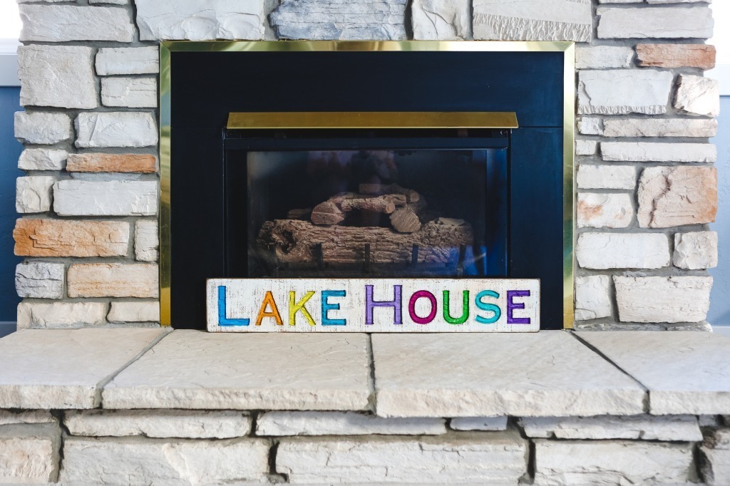 Colorful lake house sign in front of a fireplace with sandy bricks